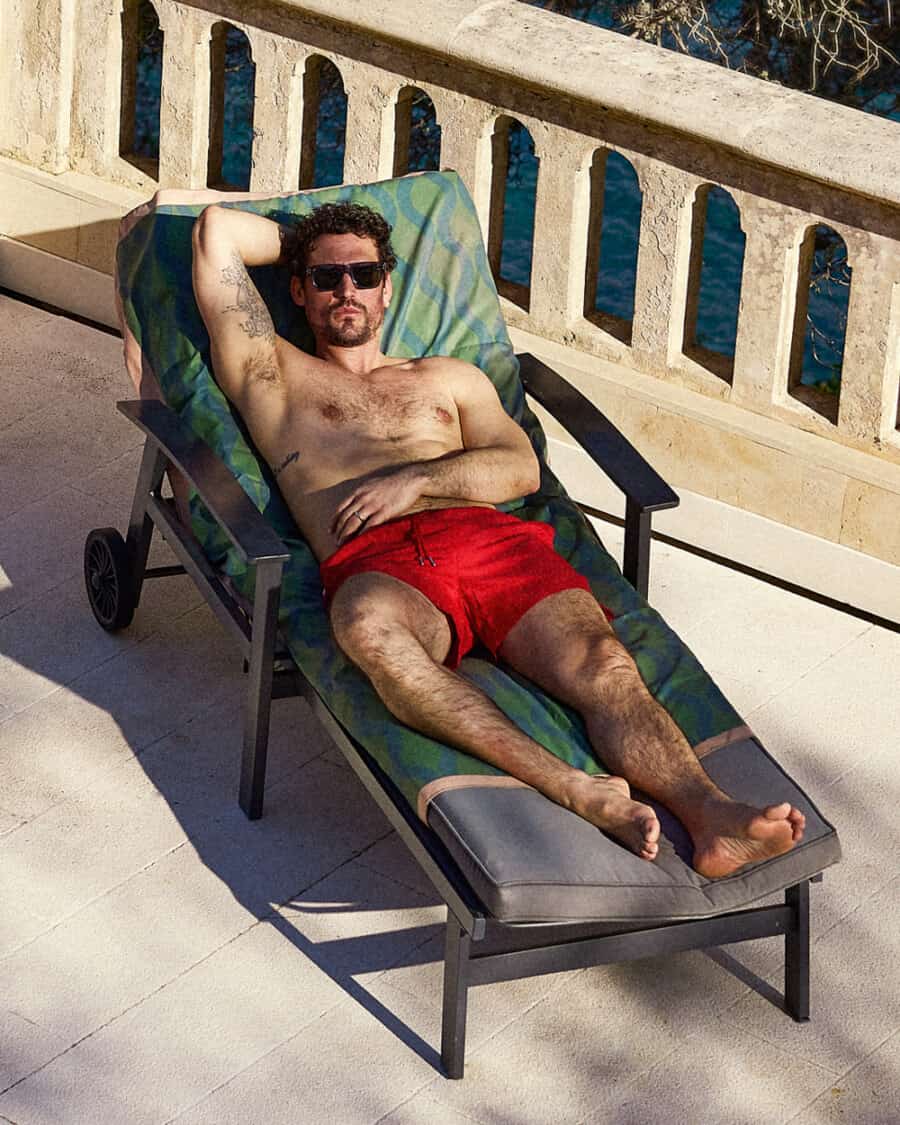 Man on sun lounger wearing primary red swim shorts