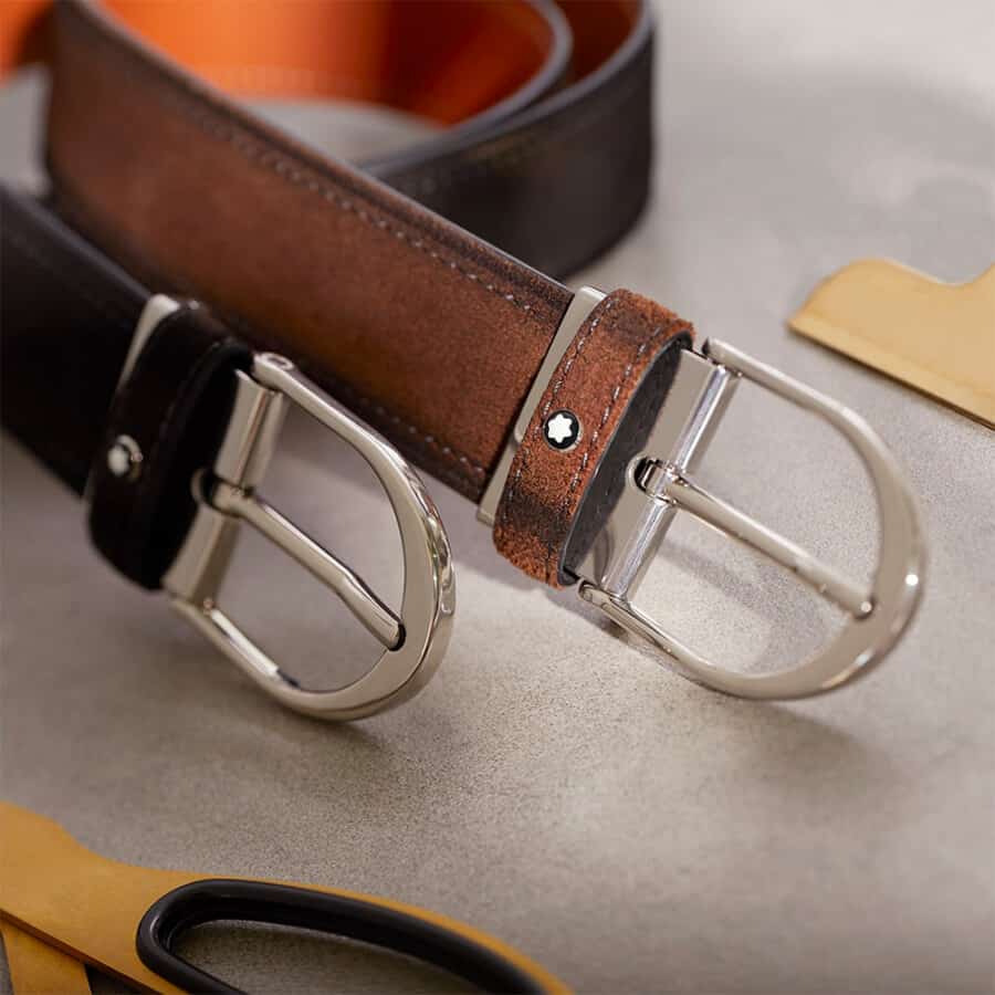 Close up of the buckles of two luxury Montblanc belts in brown and black leather