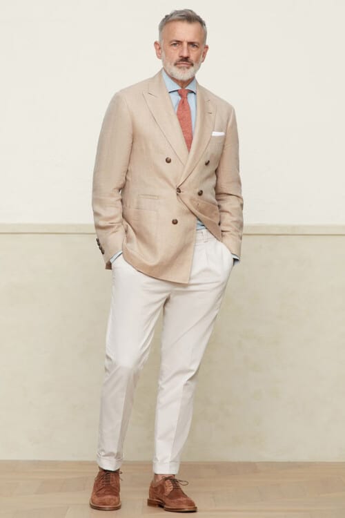 Men's white trousers, beige double-breasted blazer, light blue shirt, pink tie and brown suede Derby shoes outfit