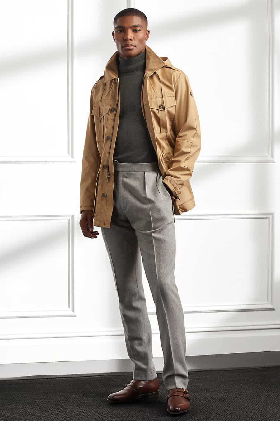 Men's grey tailored wool pants, charcoal turtleneck, brown leather double monk straps and khaki safari jacket outfit