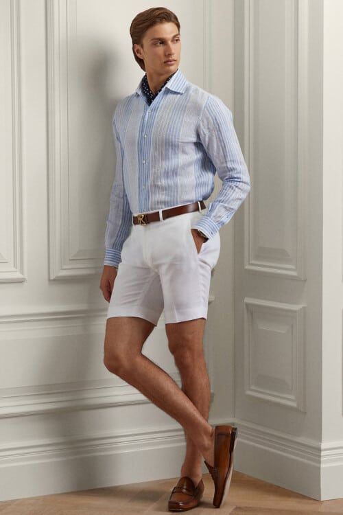 Men's white shorts, light blue stripe shirt, brown leather belt, navy cravat and brown leather penny loafers outfit