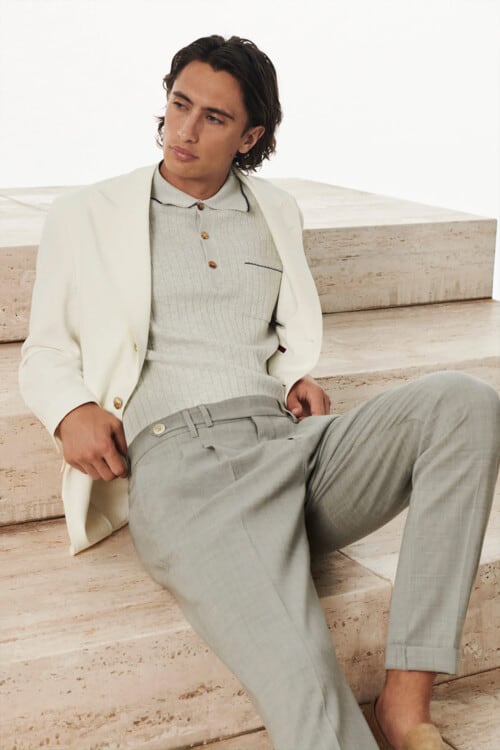 Man wearing light grey tailored pants, grey knitted polo shirt and off-white blazer