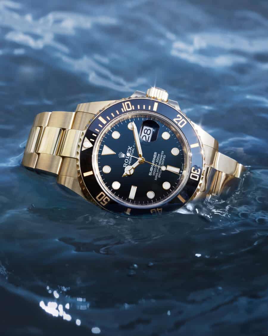 Rolex Submariner watch laying in water. Gold bracelet with black face and dial