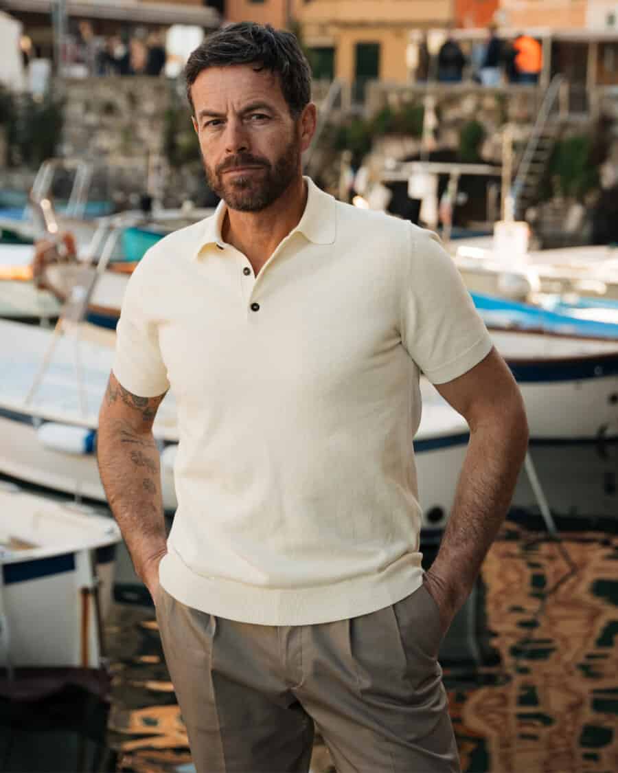 Man wearing a knitted off-white polo shirt by Velasca and pleated grey pants