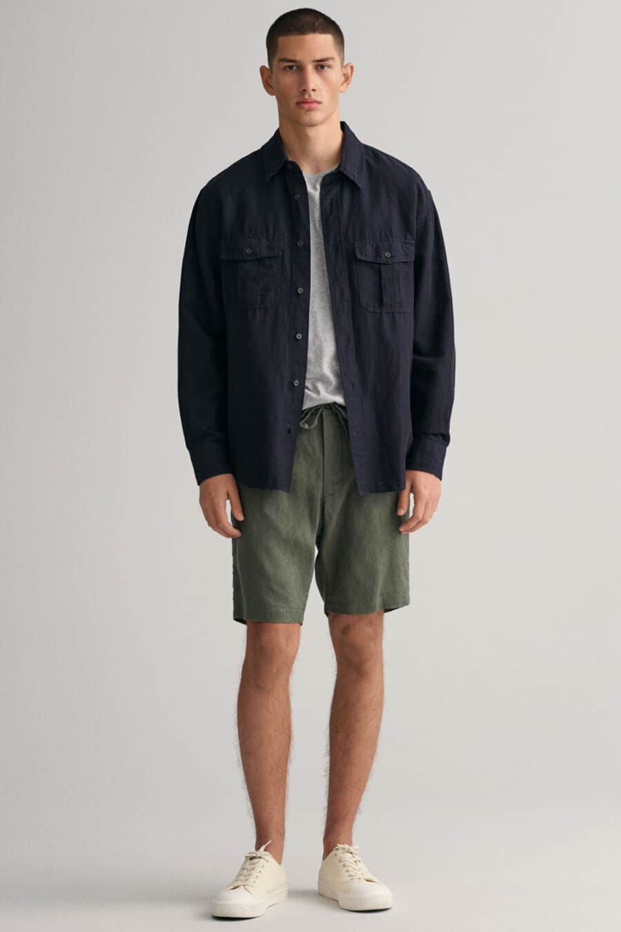 Men's green drawstring shorts, grey T-shirt, navy overshirt and off-white sneakers outfit