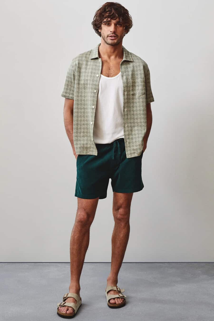 Men's teal green shorts, white vest, light green patterned shirt and beige slider sandals outfit