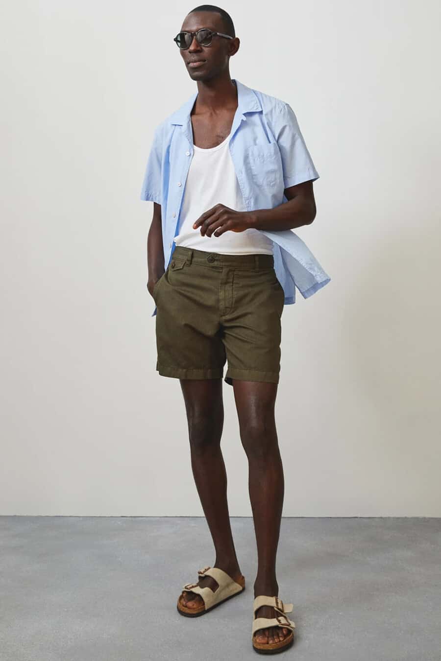 Men's dark green shorts, white vest, light blue camp collar shirt and beige slide sandals outfit