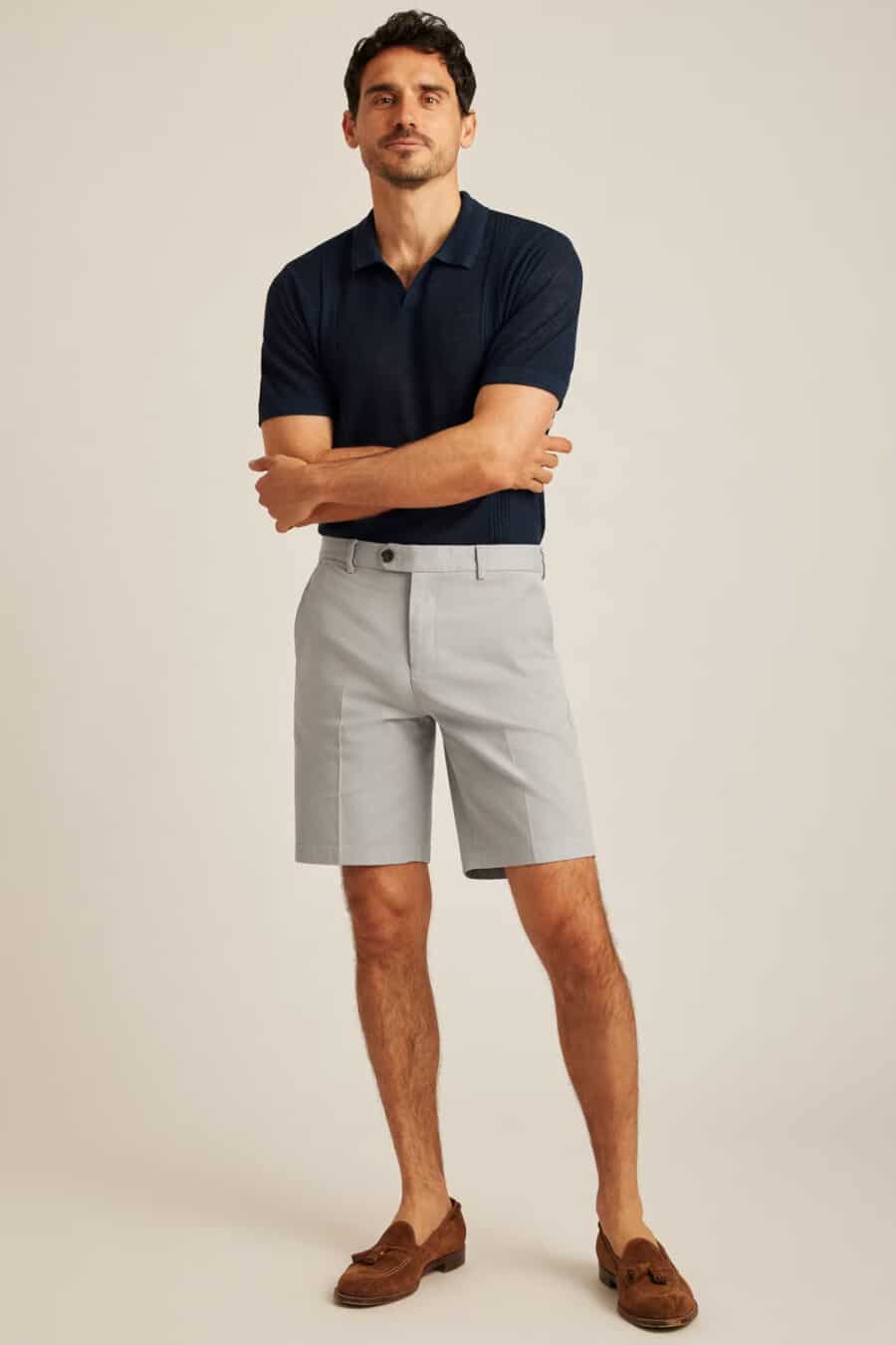 Men's navy knitted polo shirt tucked into tailored grey shorts with suede tan tassel loafers outfit
