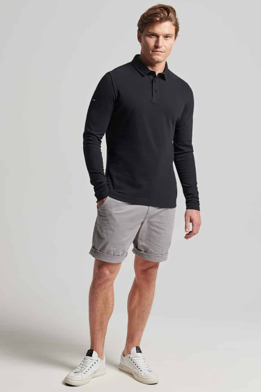 Men's grey chinos shorts, long sleeve black polo shirt and white sneakers outfit