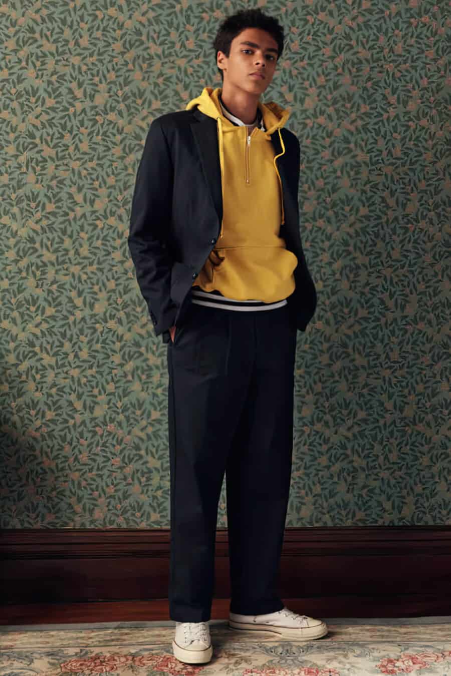 Men's navy suit, yellow hoodie and off-white canvas low top sneakers outfit