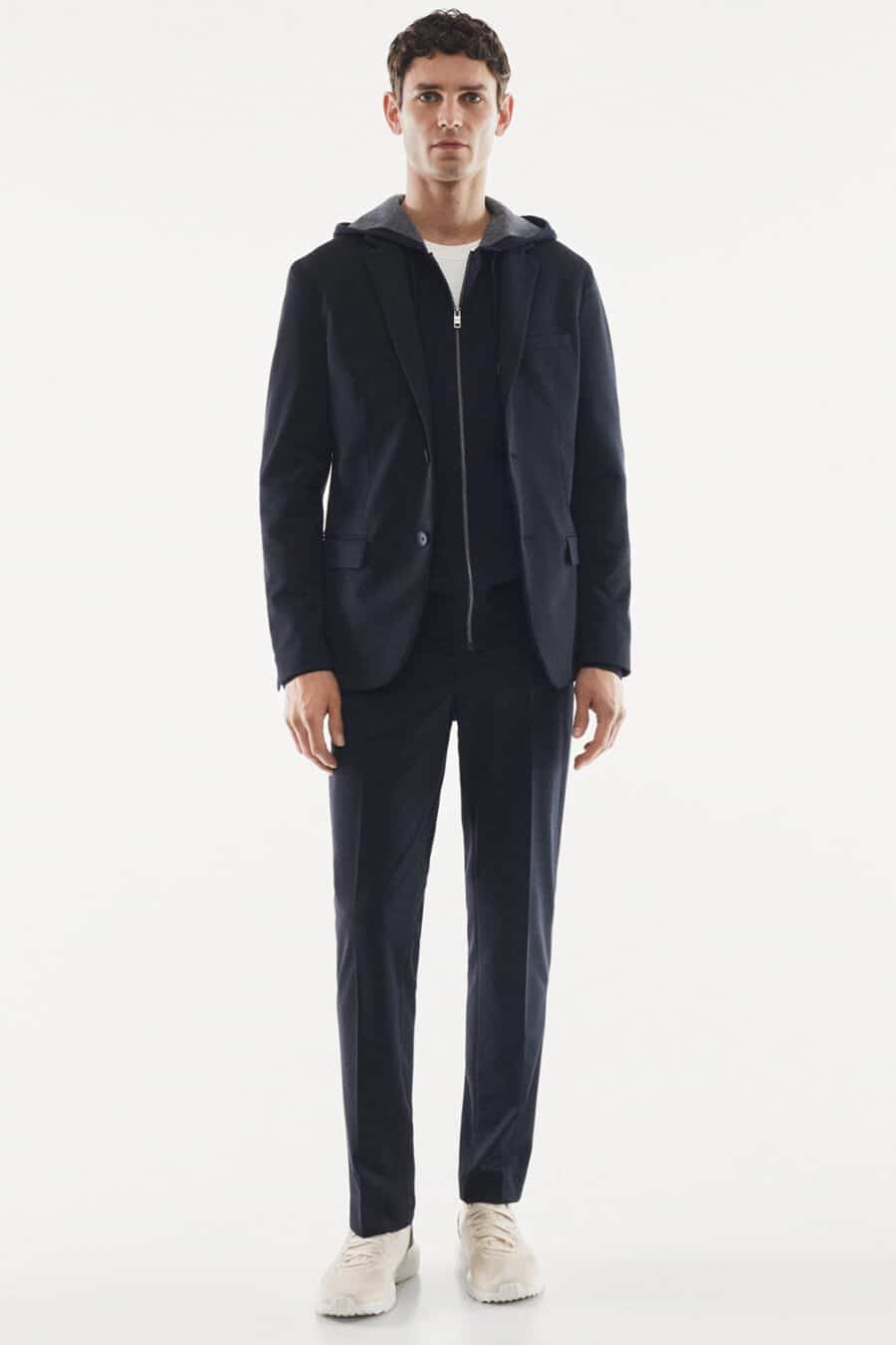 Men's navy suit, navy zip-up hoodie, white T-shirt and cream sneakers outfit