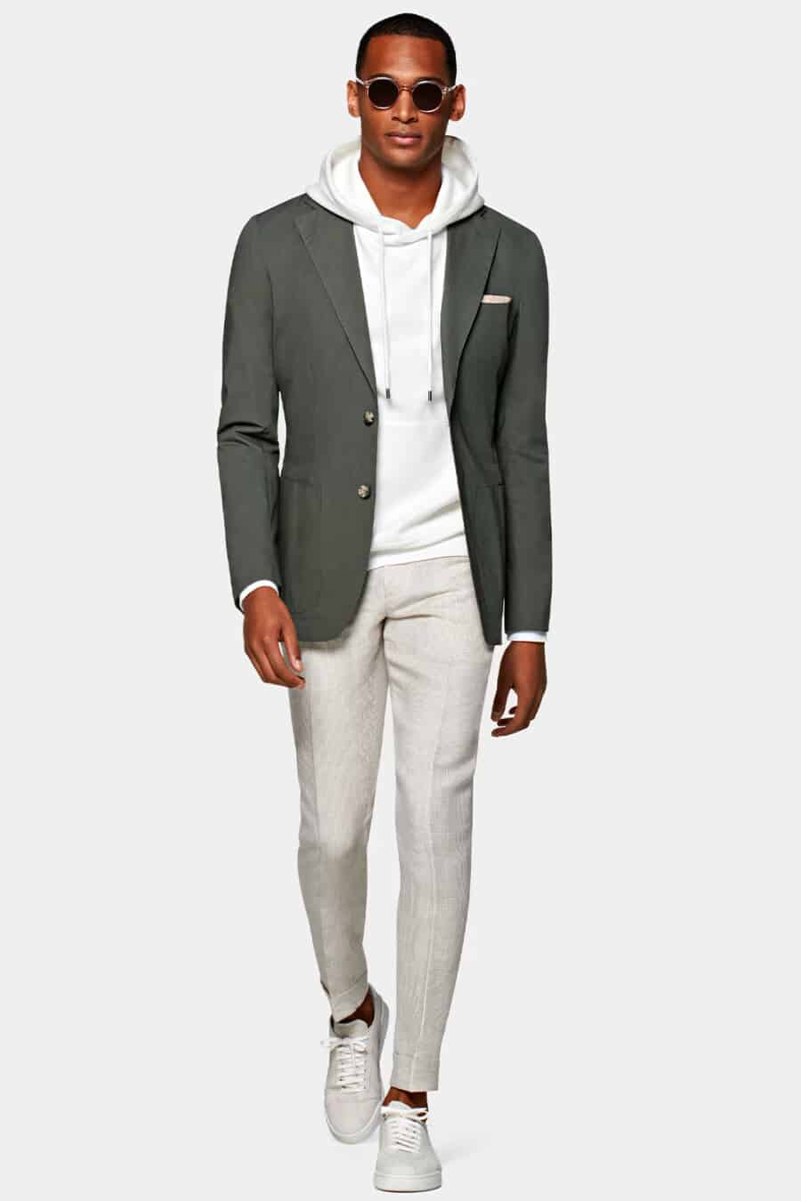 Men's grey tailored pants, white hoodie, olive green blazer, white sneakers and round sunglasses outfit