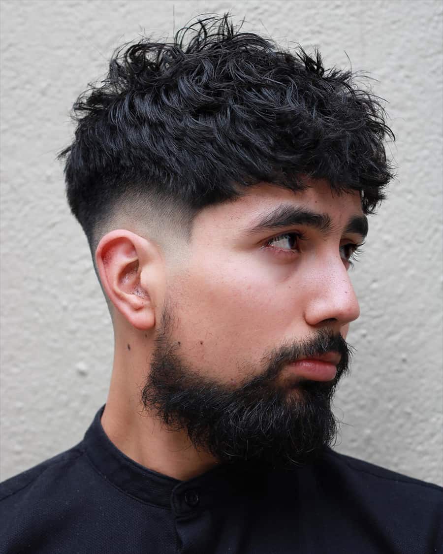 Man with black thick textured hair brushed forward messily with a low skin fade