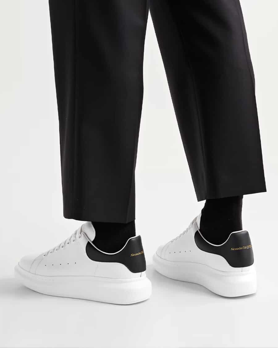 White Alexander McQueen exaggerated sole sneakers worn on feet with black socks and black cropped pants