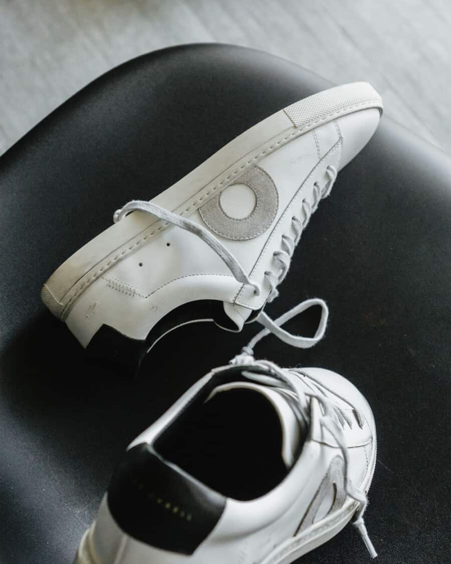 A pair of distressed Oliver Cabell white sneakers set on a black chair