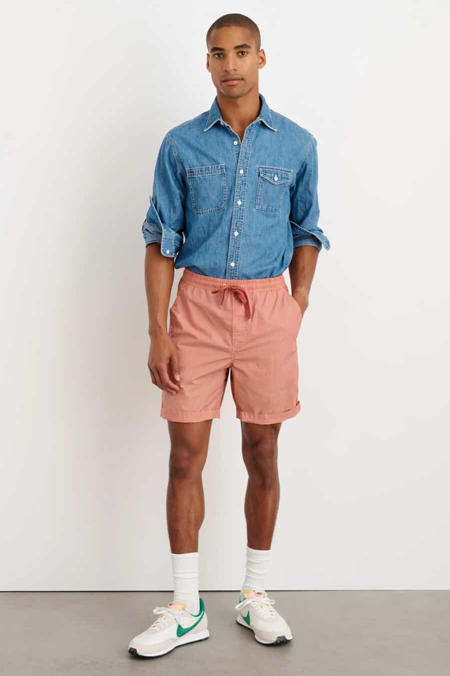 Men's coral pink shirts, tucked in mid-blue denim shirt, long white socks and Nike running sneakers outfit