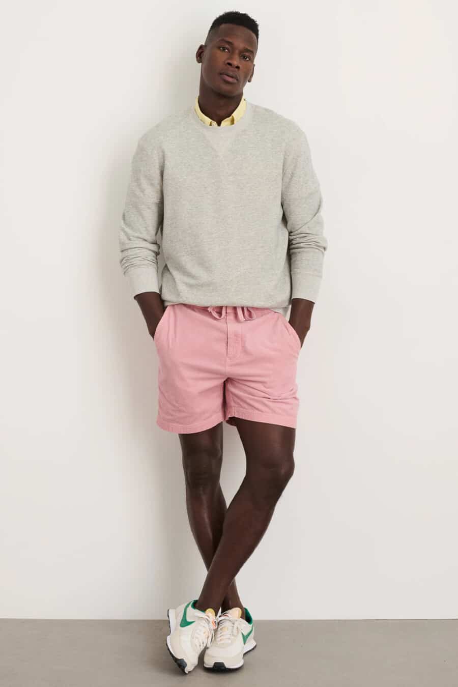 Men's pink drawstring shorts, yellow Oxford shirt, grey crew neck sweatshirt and Nike running sneakers outfit