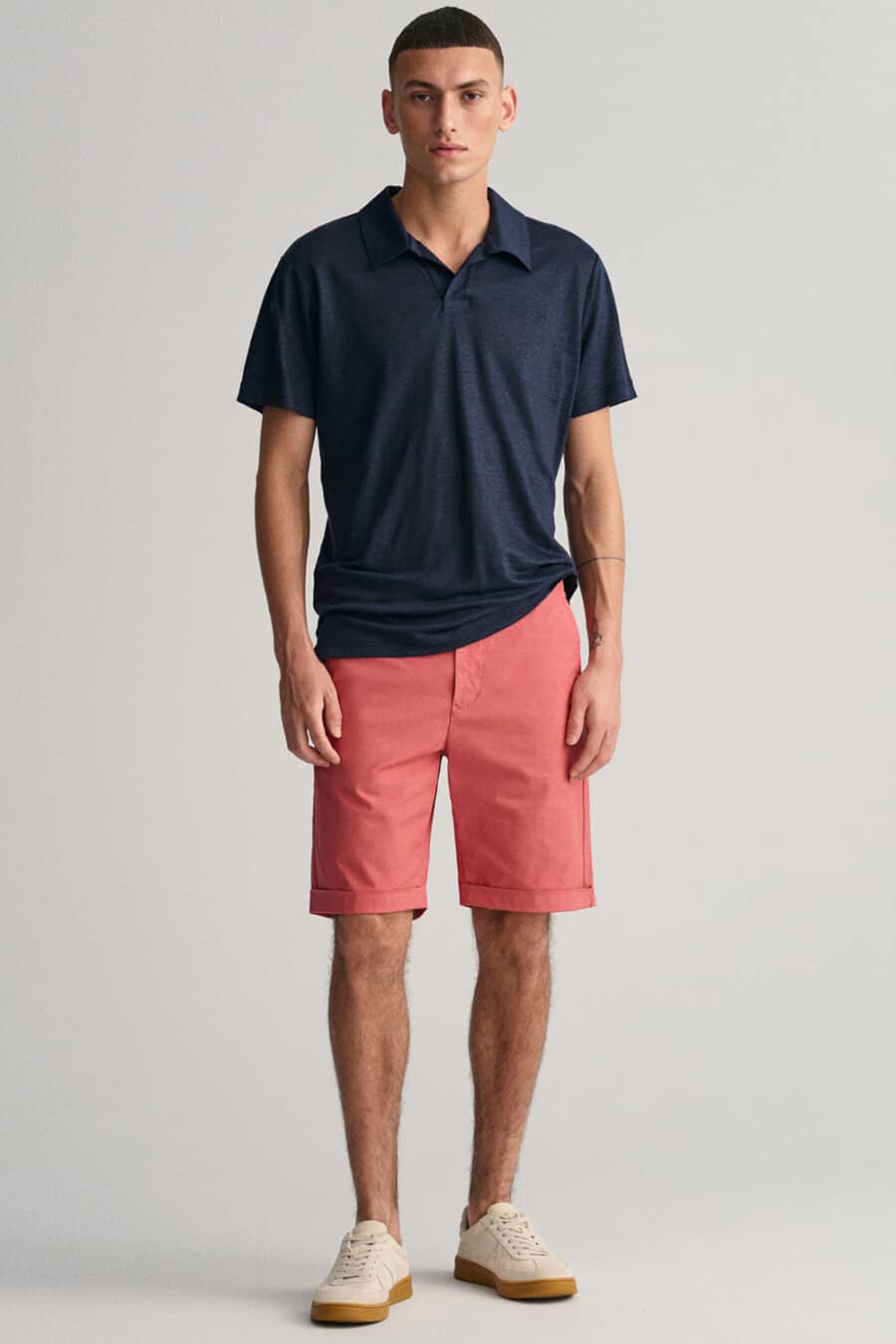 Men's coral pink chino shorts, navy polo shirt and cream gum sole sneakers outfit