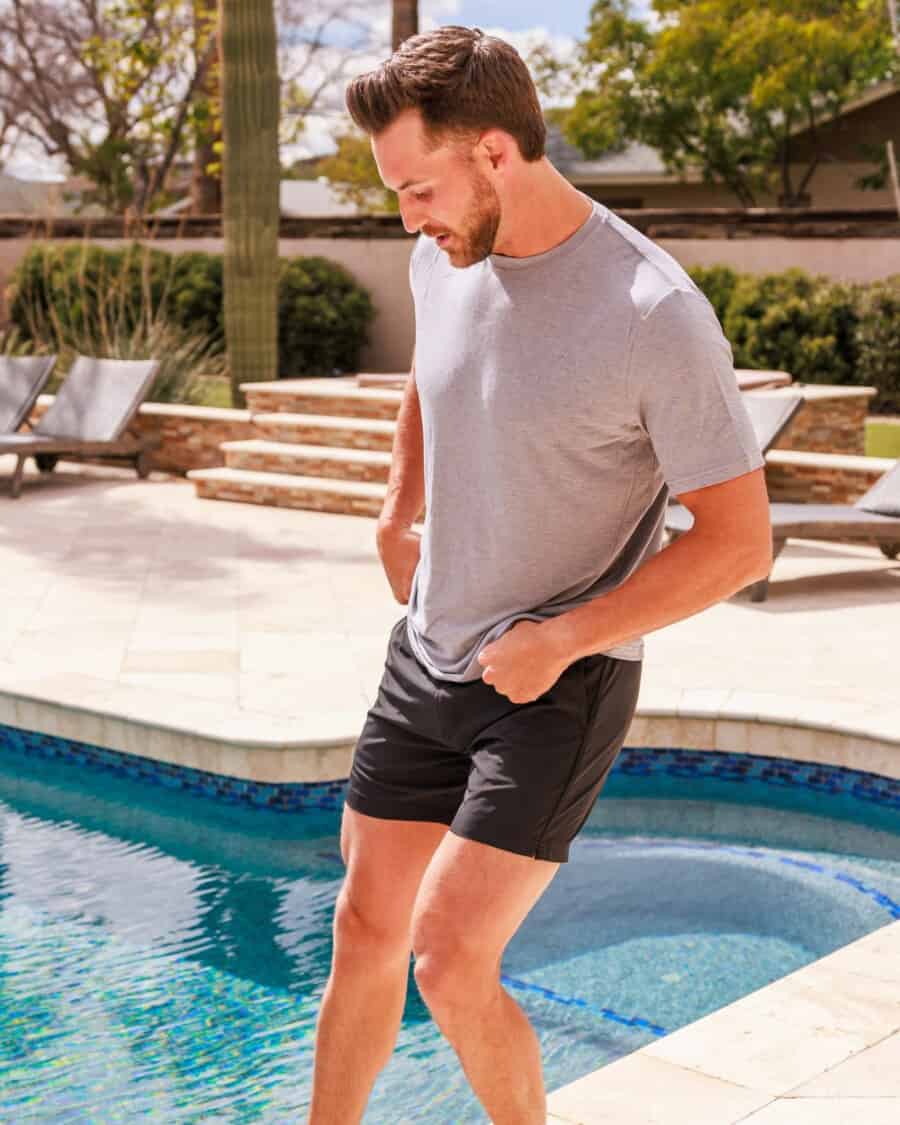 Man wearing tailored black swim shorts with a grey T-shirt on side of pool