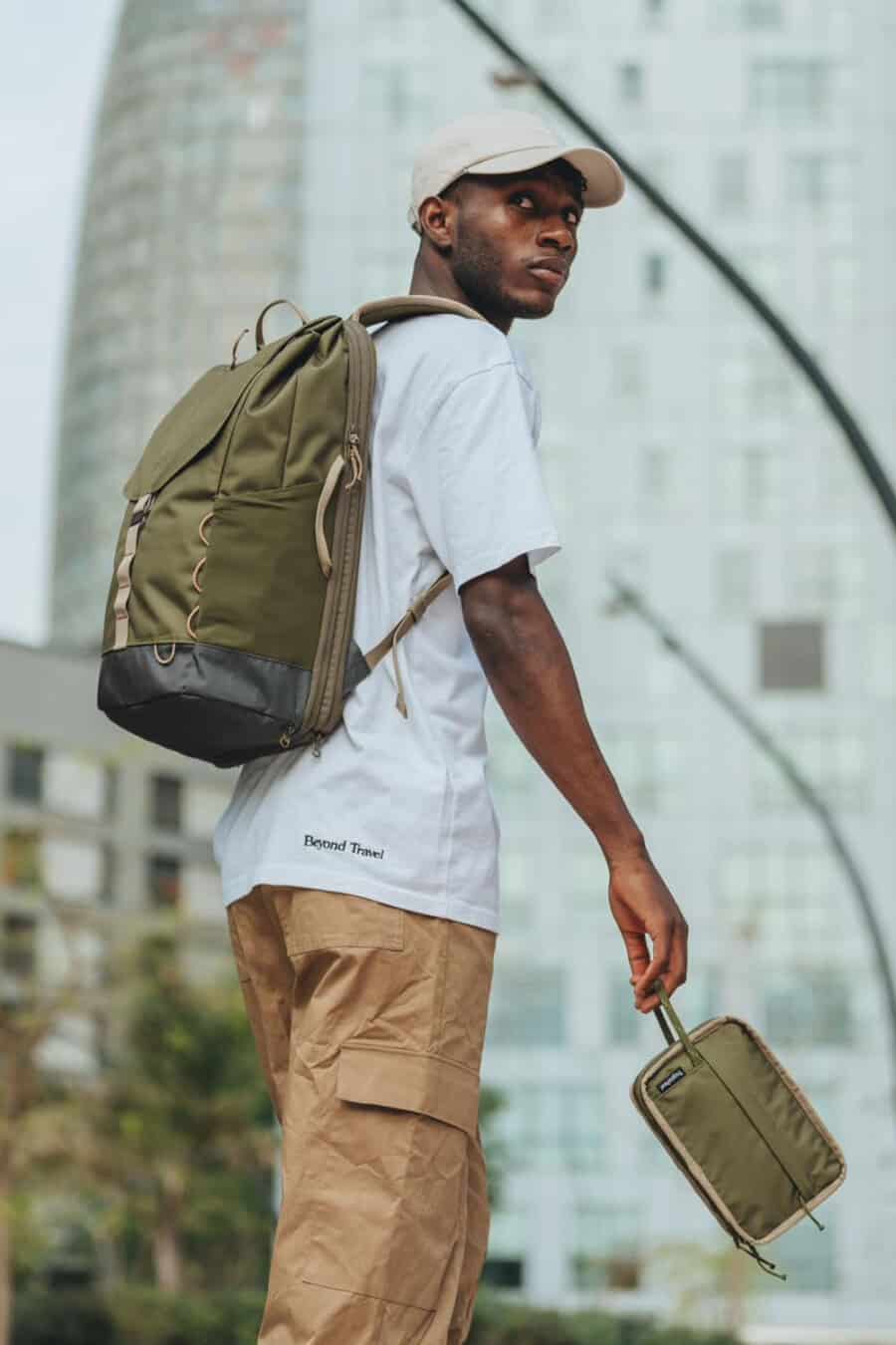 Black man wearing khaki combat pants, white T-shirt and canvas olive green backpack