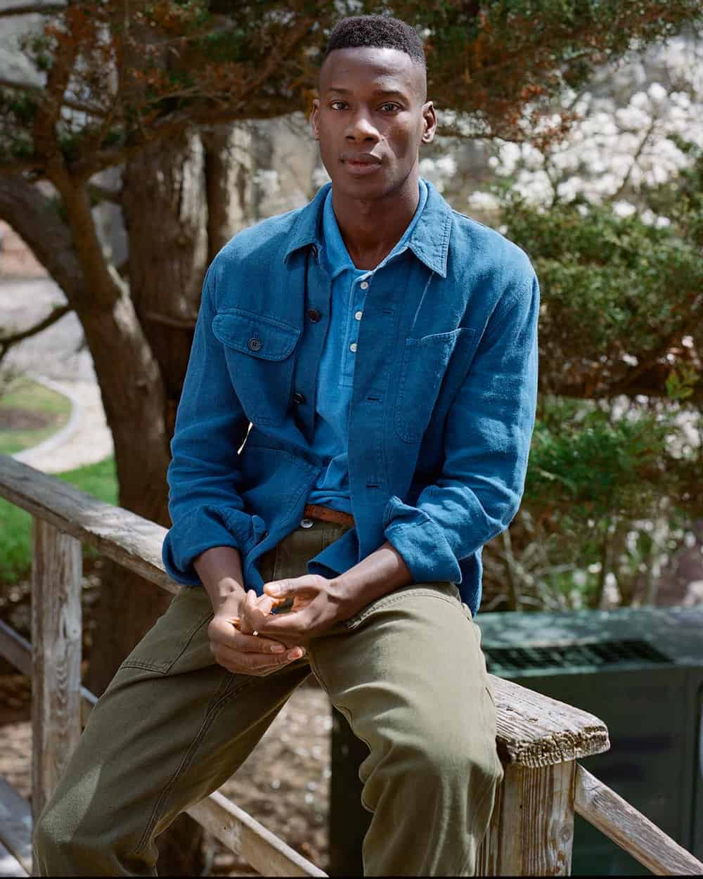 Black man wearing Alex Mill relaxed green utility pants, light blue polo shirt and washed blue patch pocket overshirt