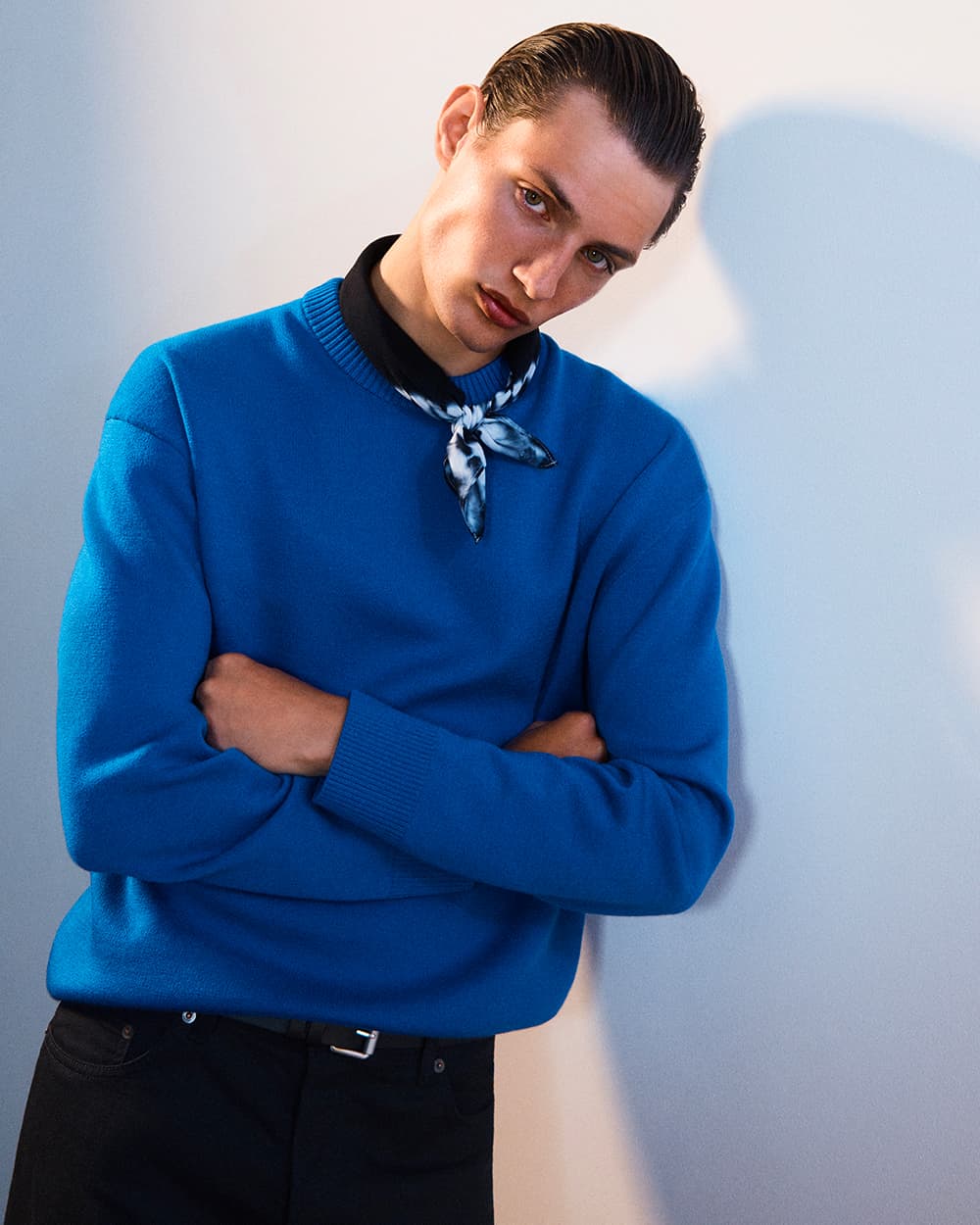 Man wearing COS bright blue sweater with black pants and a black printed neckerchief tied around neck