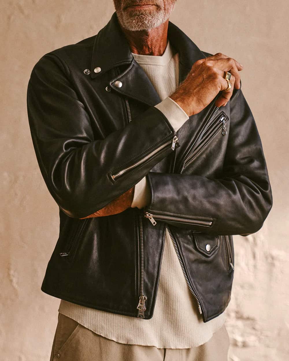 Close up of man wearing black Buck Mason leather biker jacket with an oatmeal waffle knit sweater and khaki pants