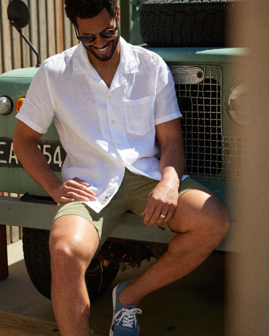 Man wearing Outerknown white short sleeve camp collar shirt, green shorts and blue canvas skate shoes