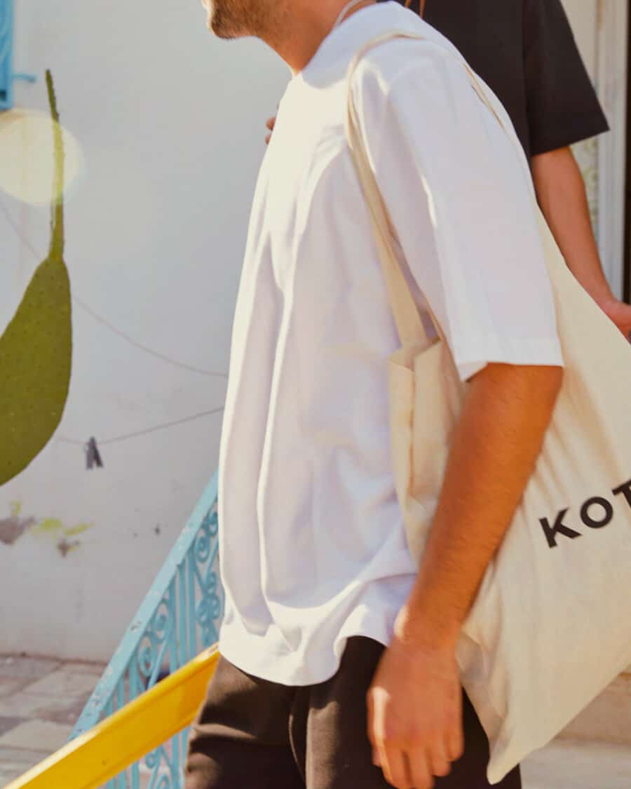 Man wearing an oversized, nicely draping white T-shirt by Kotn with black pants and a Kotn canvas tote