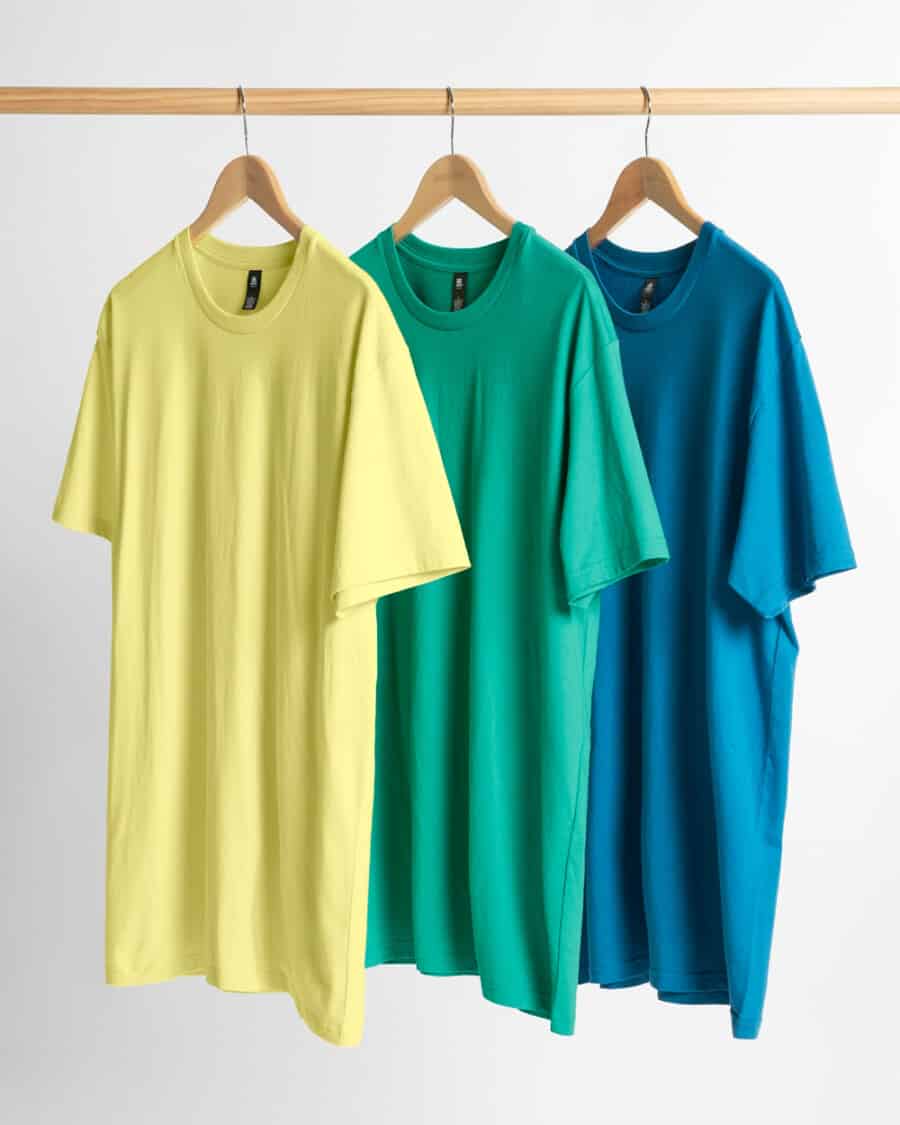 A selection of three different coloured oversized T-shirt for men by AS Colour hanging on wooden hangers