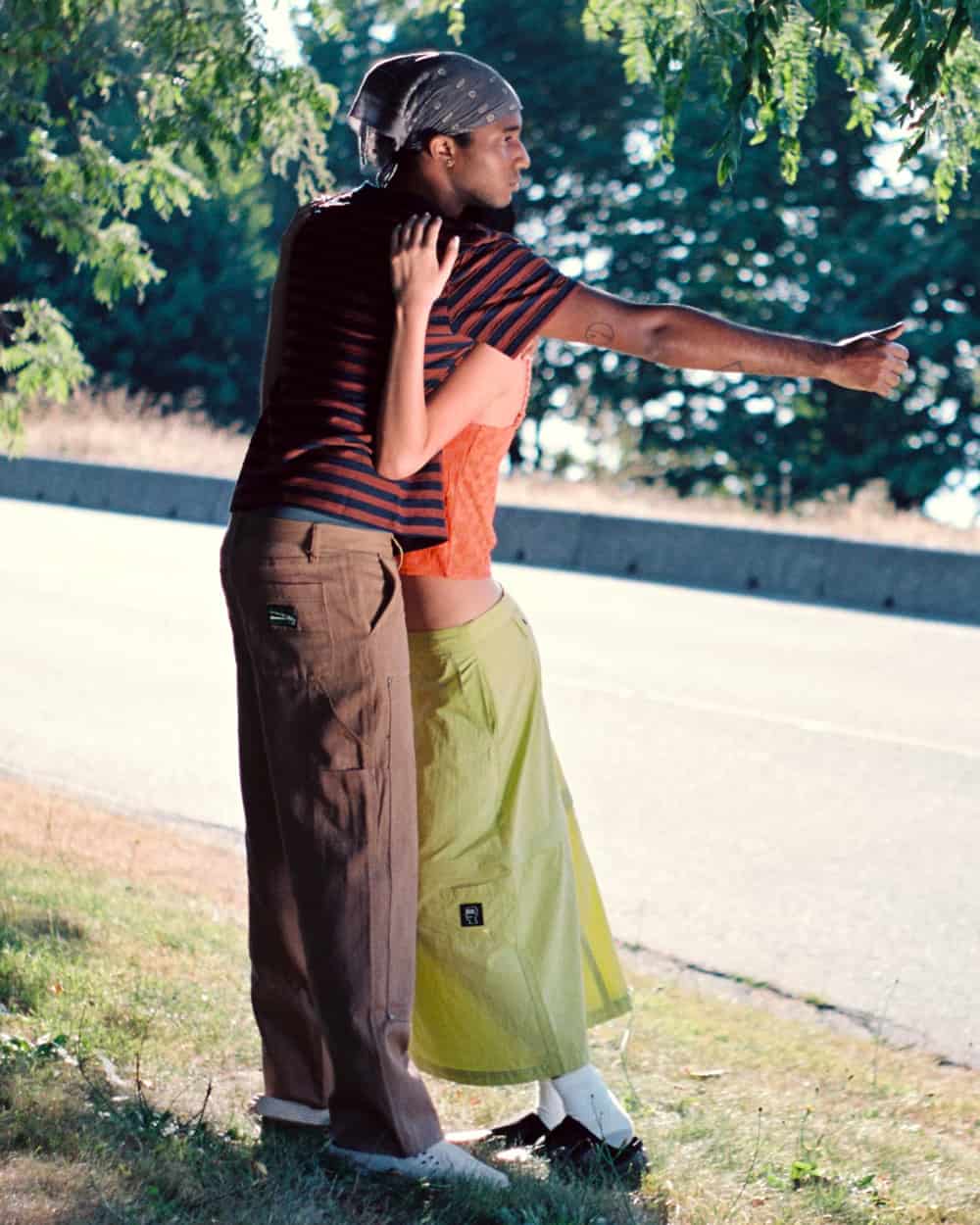 Man wearing striped Brain Dead T-shirt, brown work pants, white sneakers and bandana 