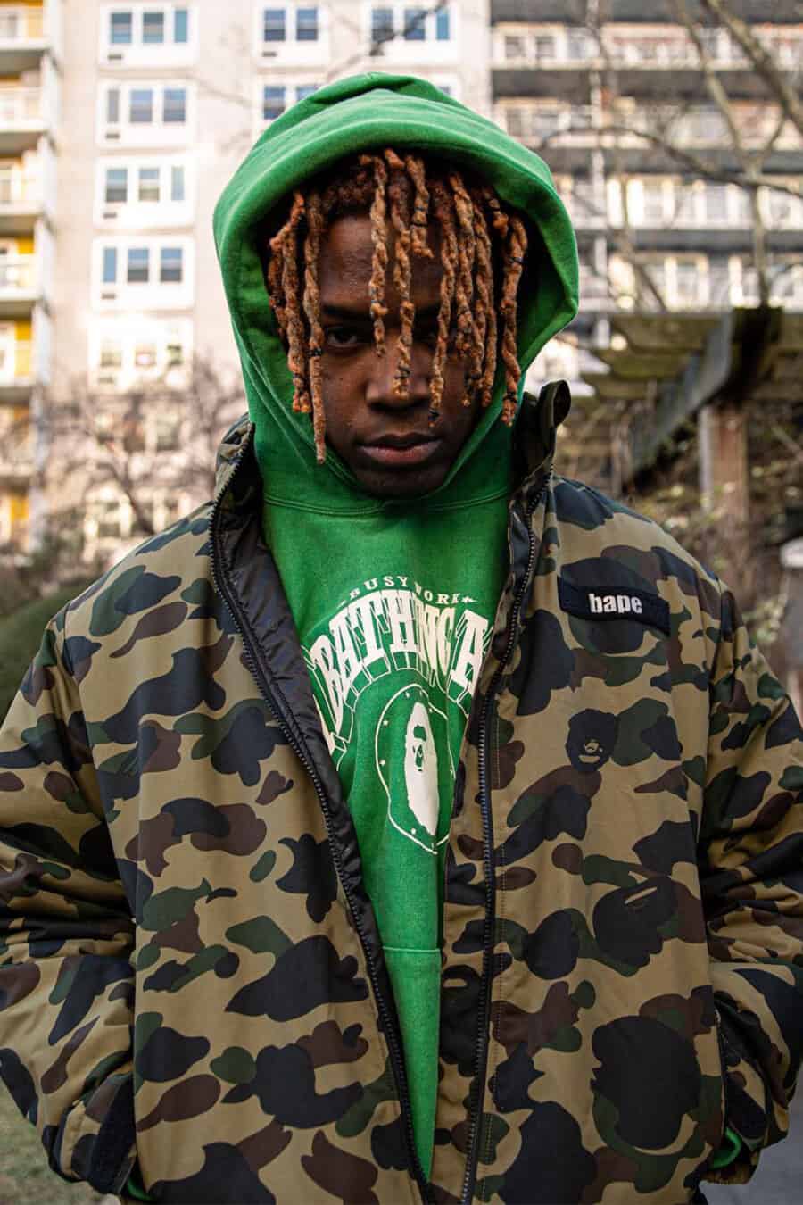 Close up of man wearing A Bathing Ape / BAPE green printed hoodie underneath a camo jacket