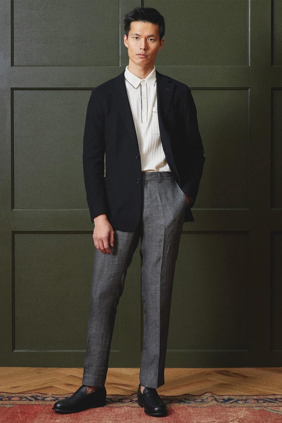 Men's tailored charcoal grey pants, white knitted polo shirt, black unstructured blazer and black leather penny loafers outfit