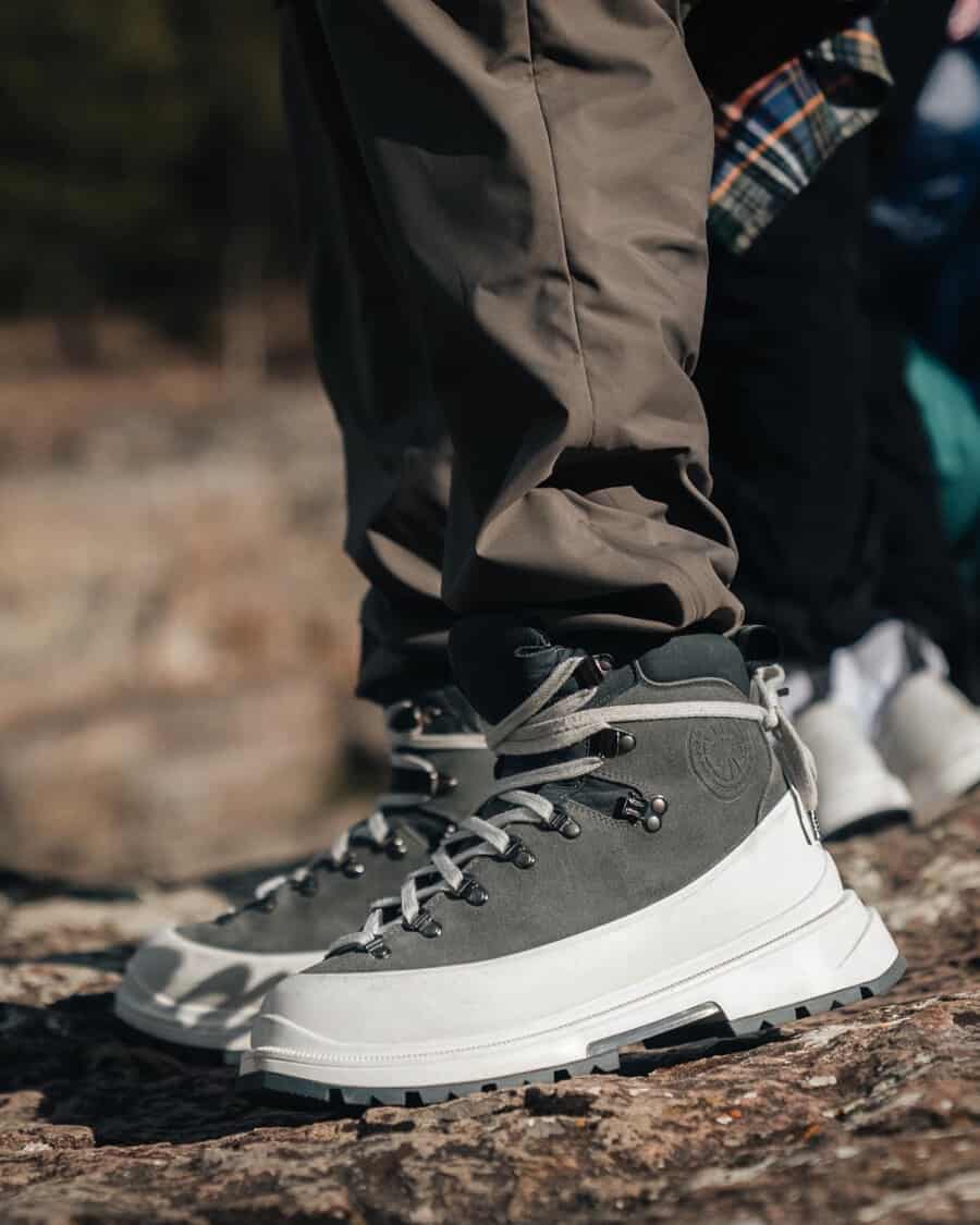 A pair of modern Canada Goose Journey hiking boots with rubber outsole worn on feet with khaki green pants