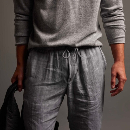 Close up of man wearing grey James Perse lightweight linen pants and a light grey cashmere sweater
