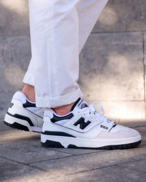 New Balance 550 white sneakers worn on feet with no socks and white pants