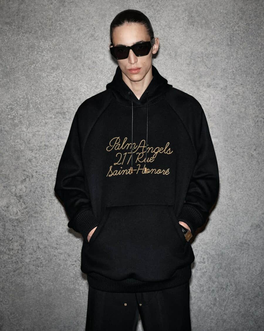 Man wearing black, oversized printed Palm Angels hoodie with black pants and sunglasses