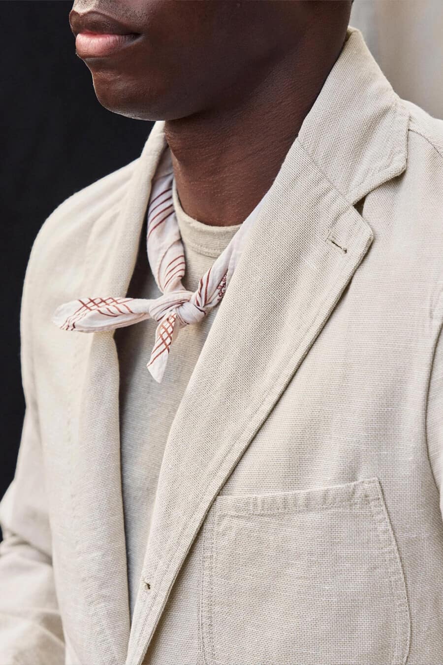 Close up of a man wearing a lightweight unstructured beige suit with a tonal tie and neckerchief