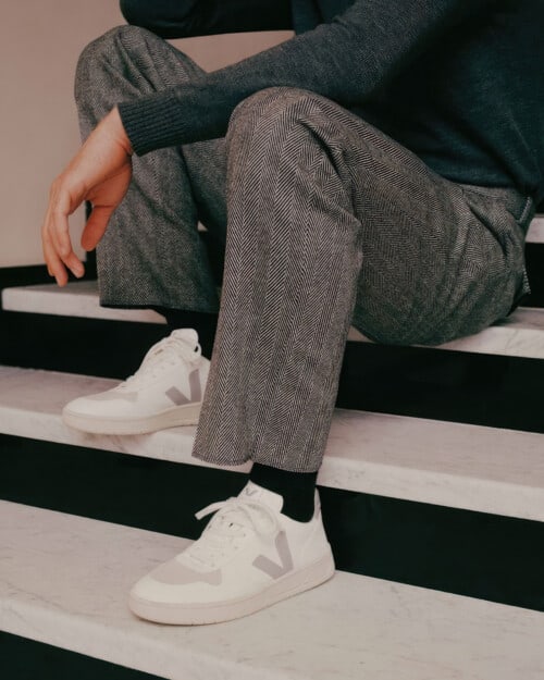 Men's VEJA V-10 CWL white sneakers worn on feet with tailored grey pants, black socks and charcoal sweater