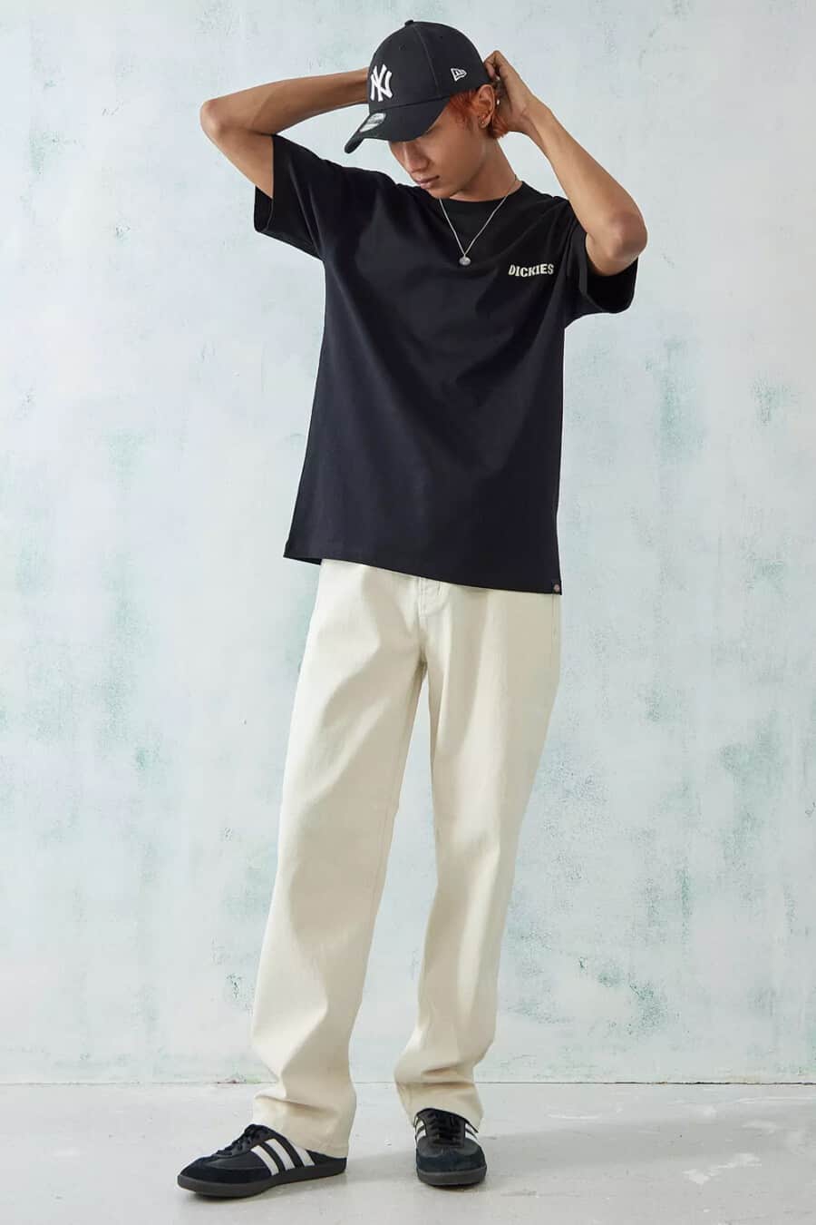 Men's baggy off-white jeans, black Dickies T-shirt, black NY Era baseball cap and black adidas Samba sneakers with pendant chain outfit