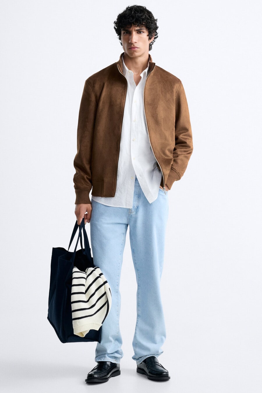Men's light blue baggy jeans, white shirt, tan suede jacket, black Derby shoes and black tote bag outfit