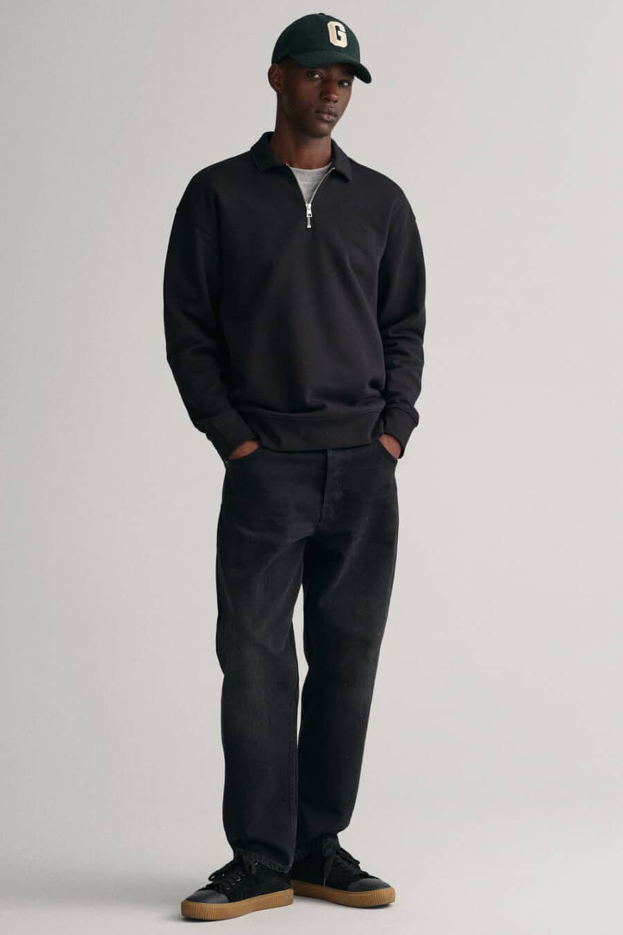 Men's black baggy jeans, grey T-shirt, black quarter-zip sweater and black gum sole sneakers outfit