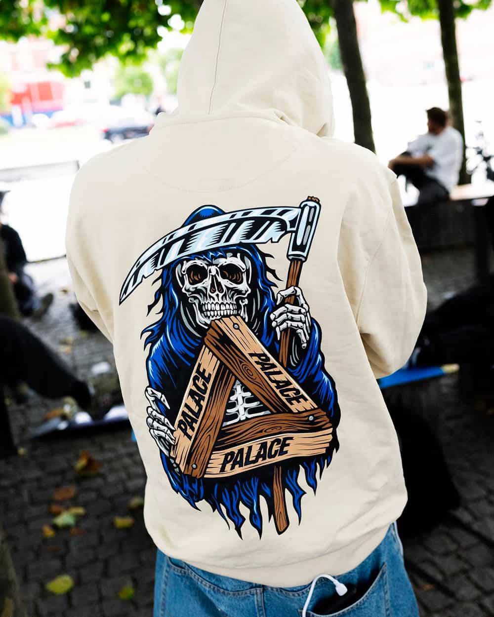 Rear of an off-white grim reaper printed Palace Skateboards hoodie worn with baggy light wash jeans