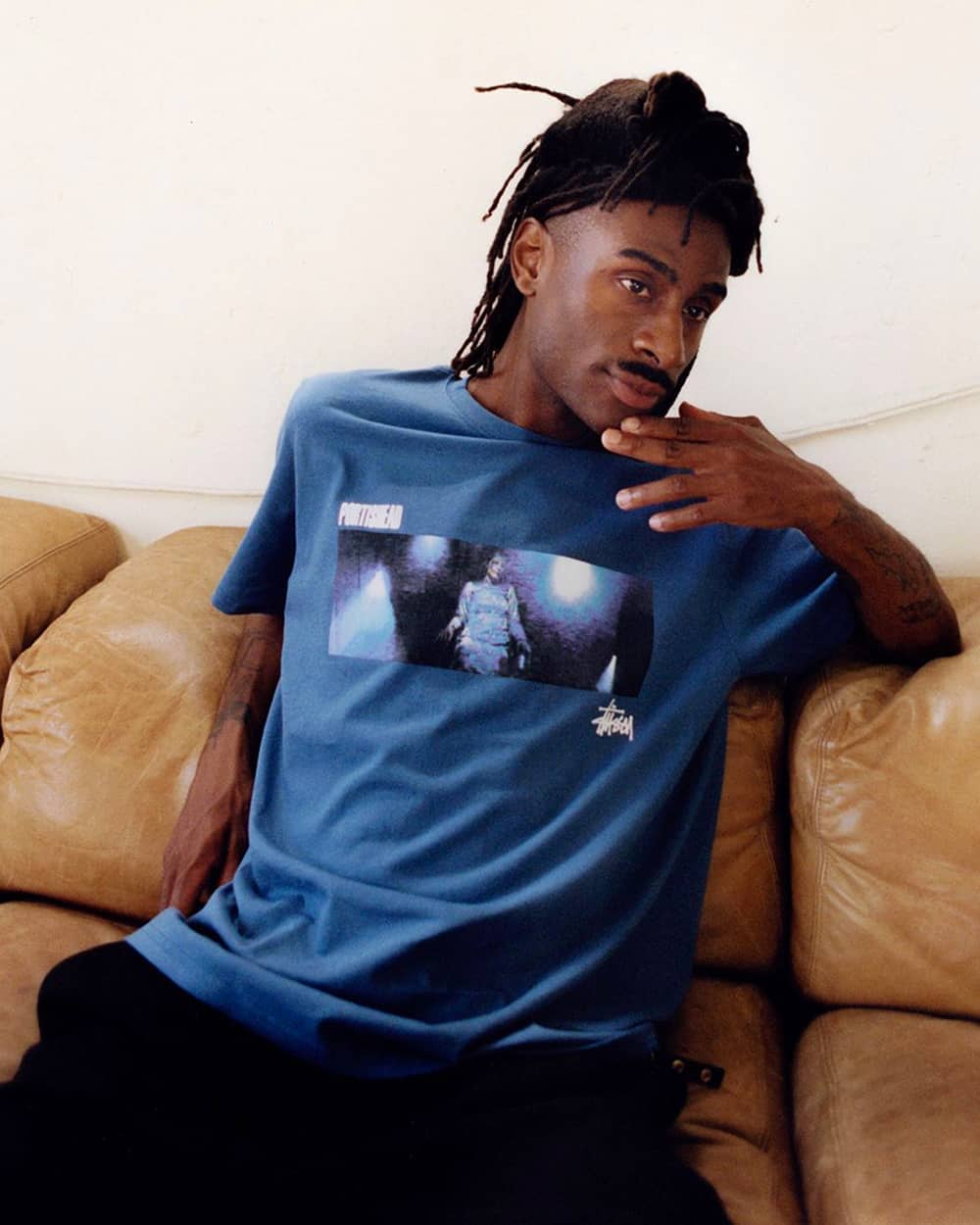 Black man wearing printed blue Stussy T-shirt and loose black pants