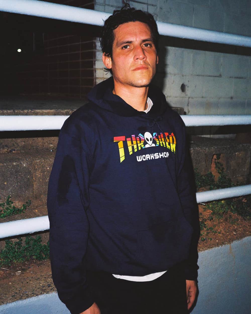 Man wearing navy Thrasher x Alien Workshop logo hoodie with a white T-shirt and black pants