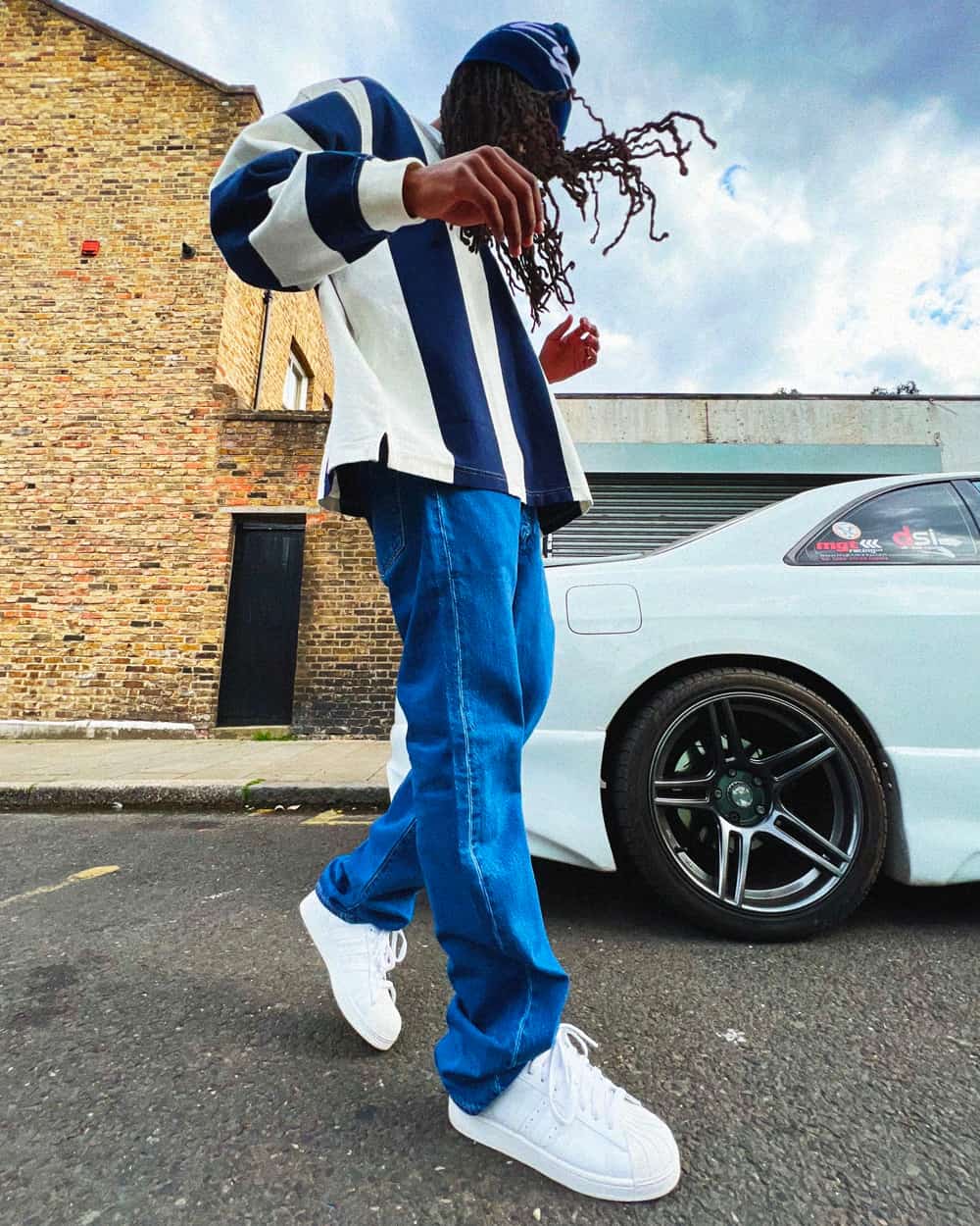 Man wearing loose mid wash denim jeans and a striped white/blue sweatshirt by Levi’s with chunky white sneakers