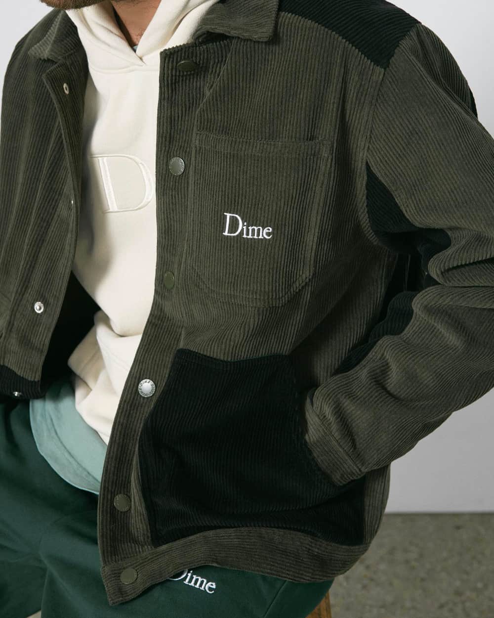 Close up of man wearing white logo hoodie, greed cord shacket and green sweatpants, all by Dime