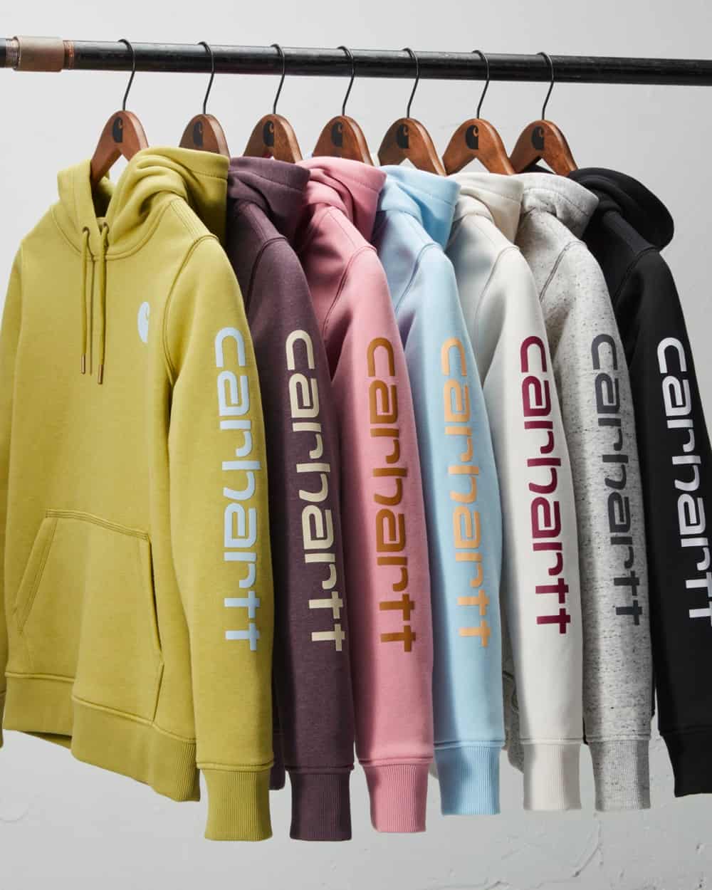 Seven Carhartt hoodies hanging on a rail in multiple colours
