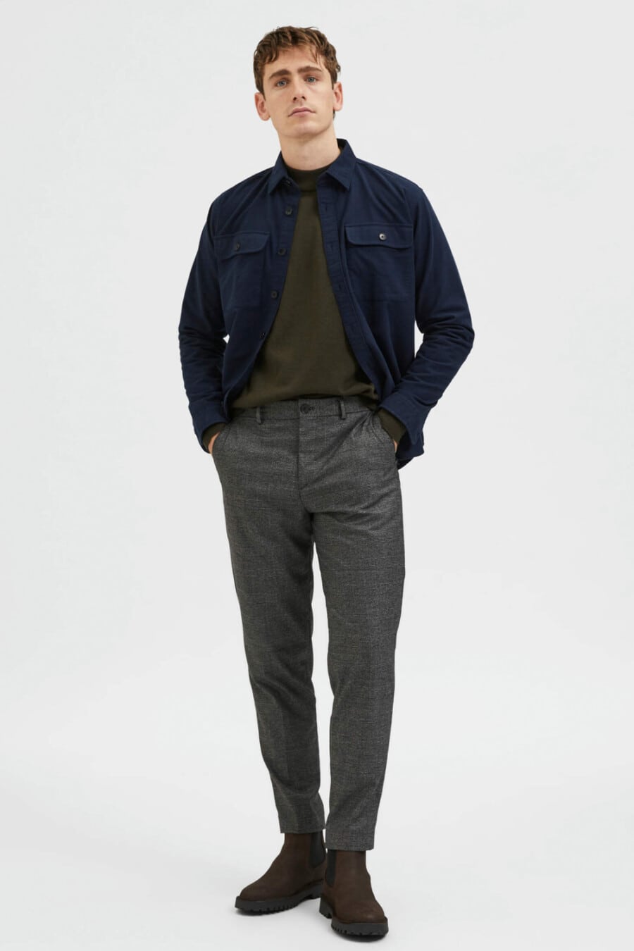 Men's grey wool pants, green long-sleeve top, navy blue shacket and brown chunky leather Chelsea boots outfit