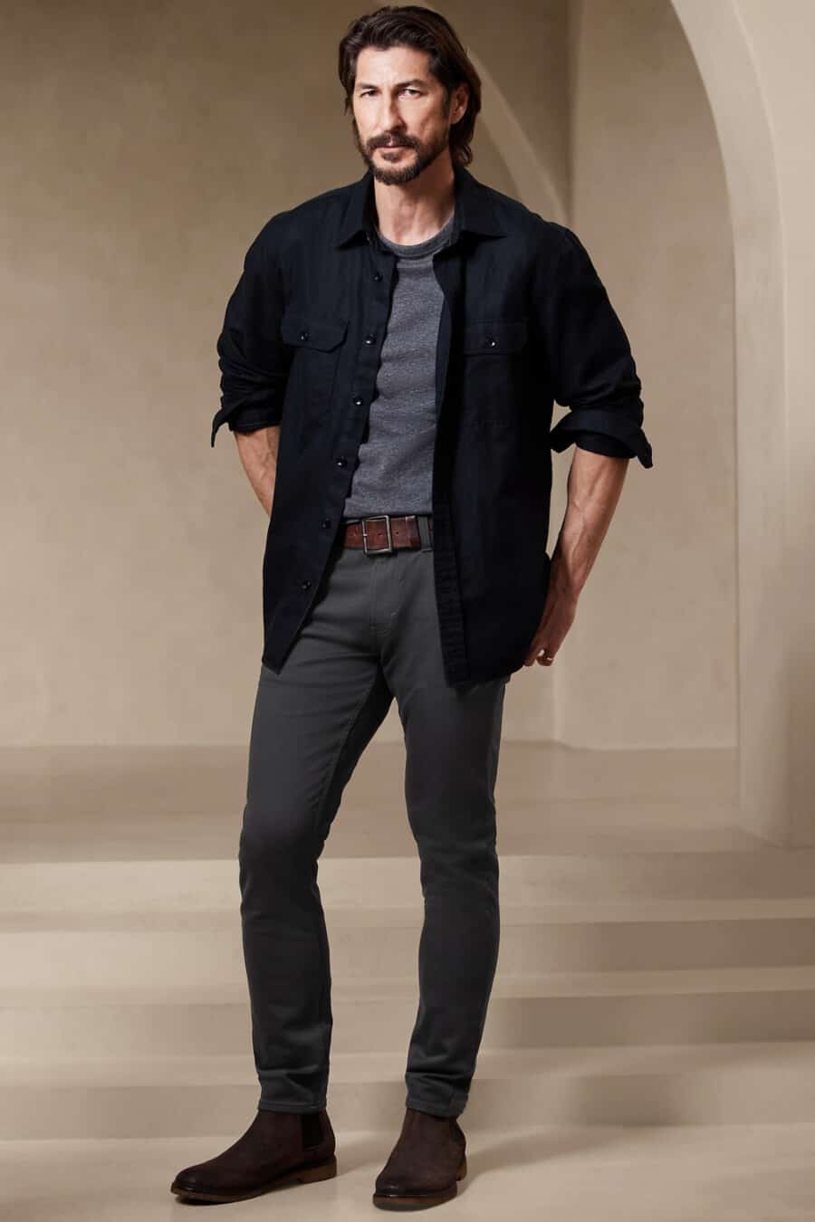 Men's charcoal chinos, dark grey T-shirt, black oversized shacket, brown leather belt and brown suede Chelsea boots outfit